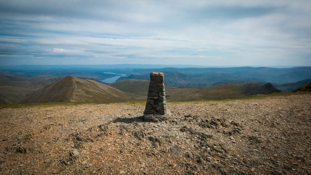 The trig point and summit of Helvellyn, with Ullswater clearly visible in the distance.